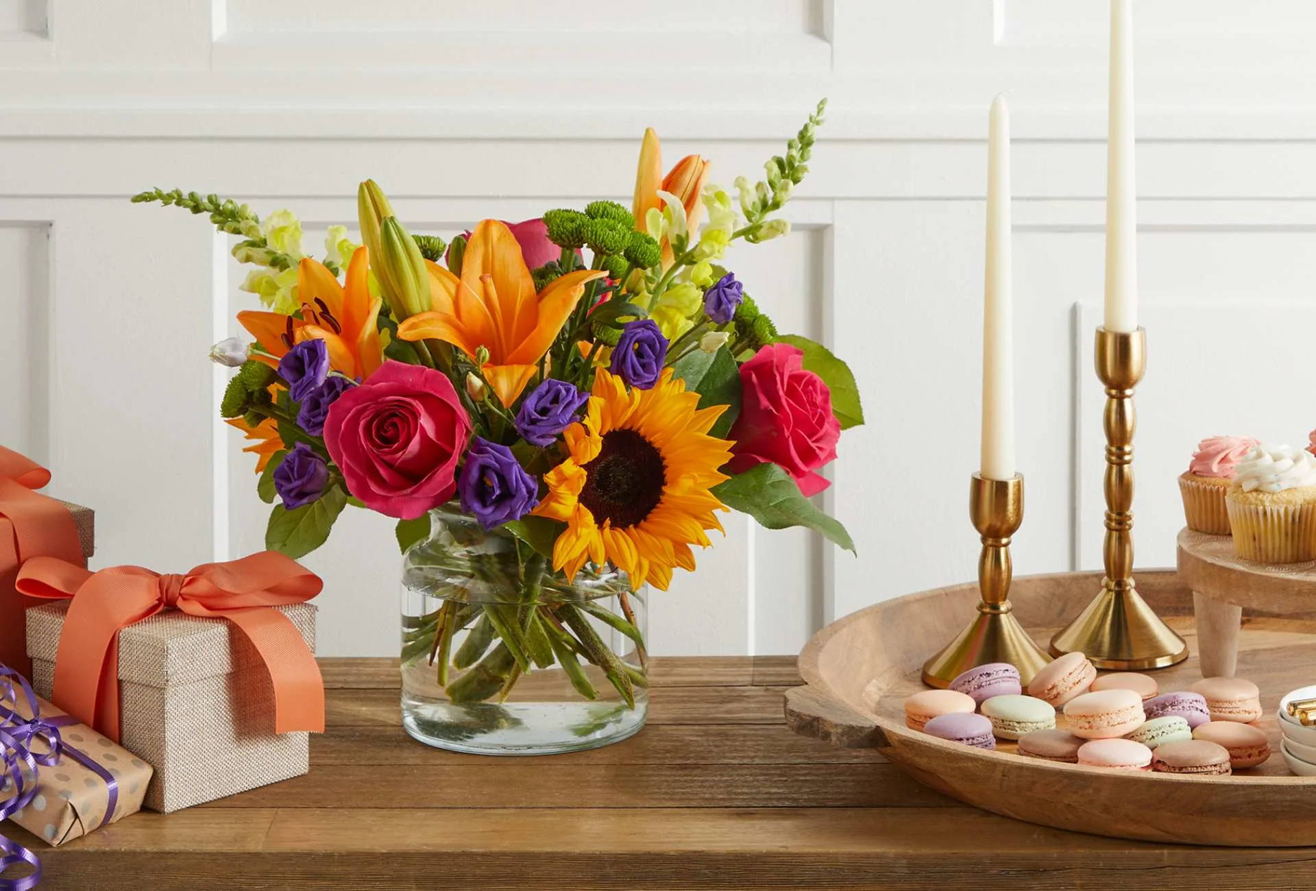 Brown tablescape featuring a multicolored flower bouquet, candelabras, a dessert tray, and gift wrapped packages