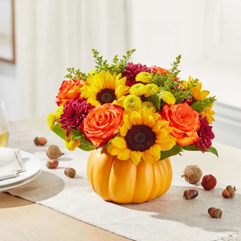 red, orange, and yellow bouquet inside a pumpkin vase sitting on a fall tablescape