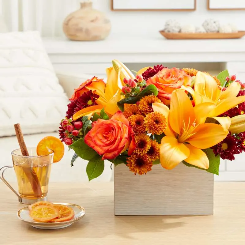 orange bouquet in a rectangular vase, sitting on a wooden table in a living room